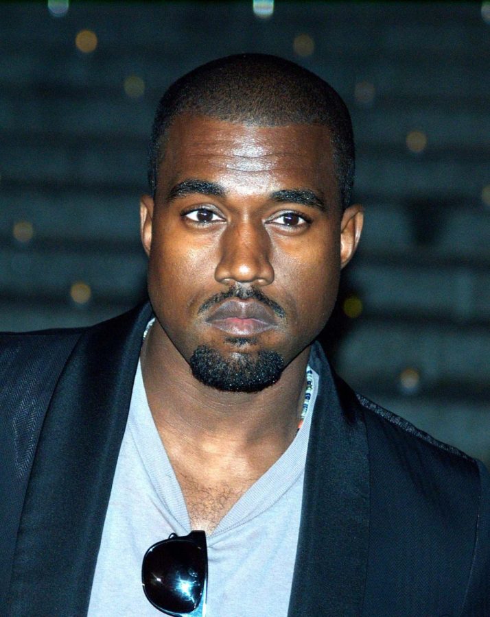 Photo of Ye West in an onyx blazer, a baby blue shirt, and sunglasses. 